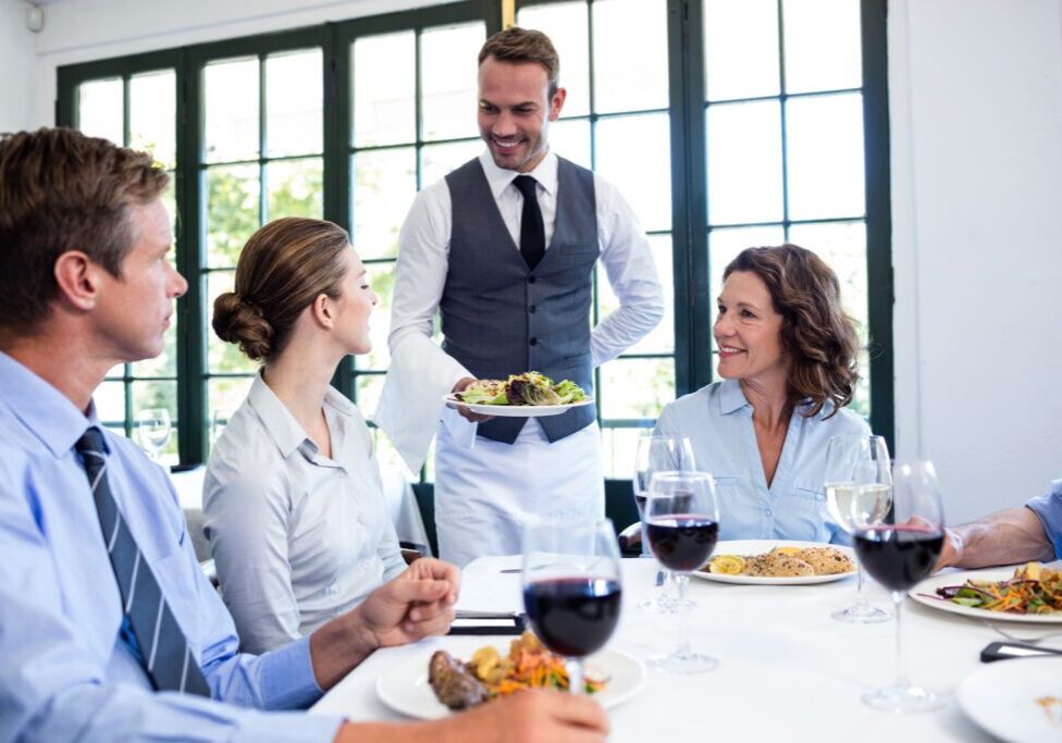 Waiter serving salad to the business people in restaurant